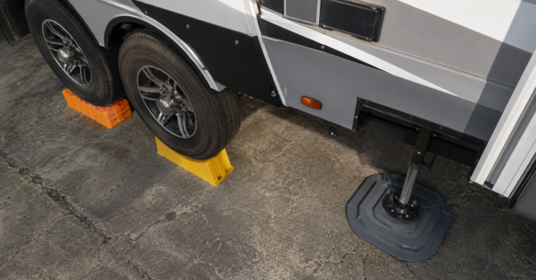 RV leveling blocks, wheel chock, and jack pad stabilizer deployed on concrete campground — complete RV leveling and stabilization setup